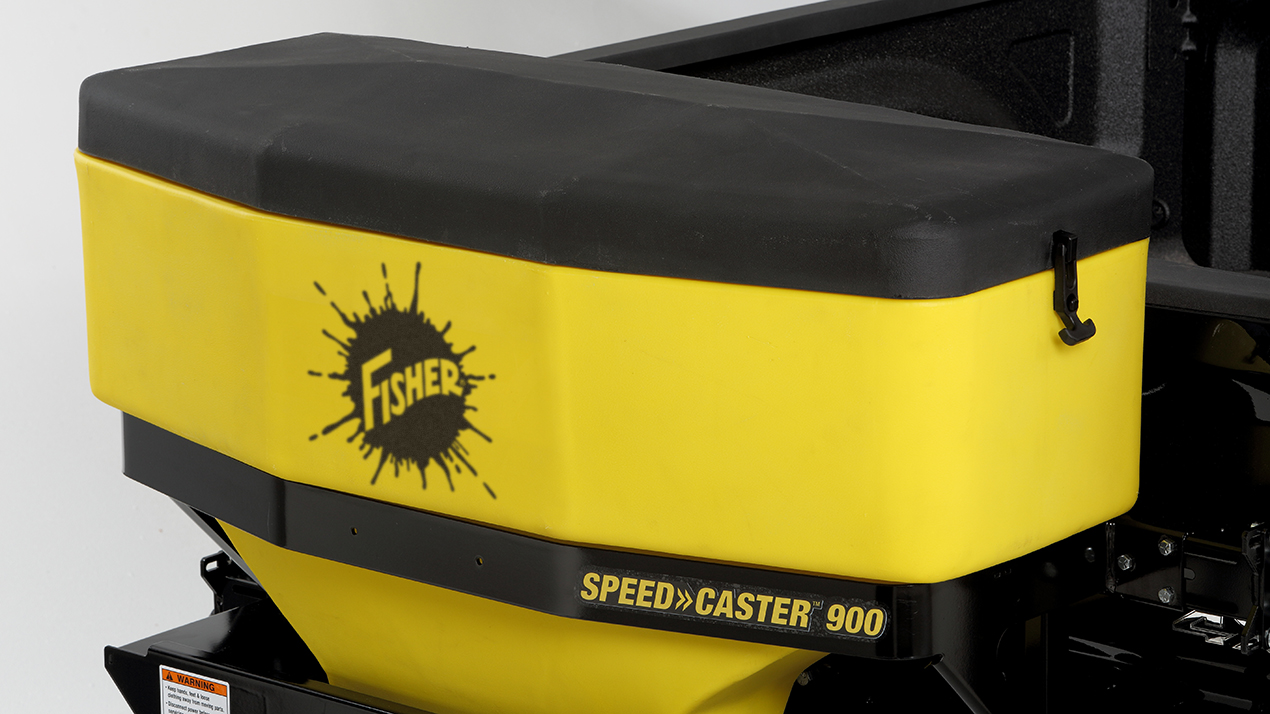 A yellow and black Fisher Speed-Caster 900 salt spreader is mounted on the back of a vehicle, with the Fisher logo displayed on the side.