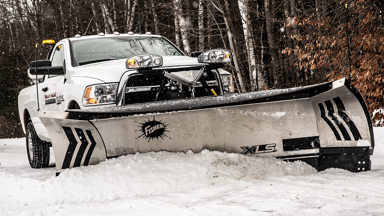 A white pickup truck equipped with a large silver snowplow clears snow from a road, surrounded by trees in a snowy, winter landscape.