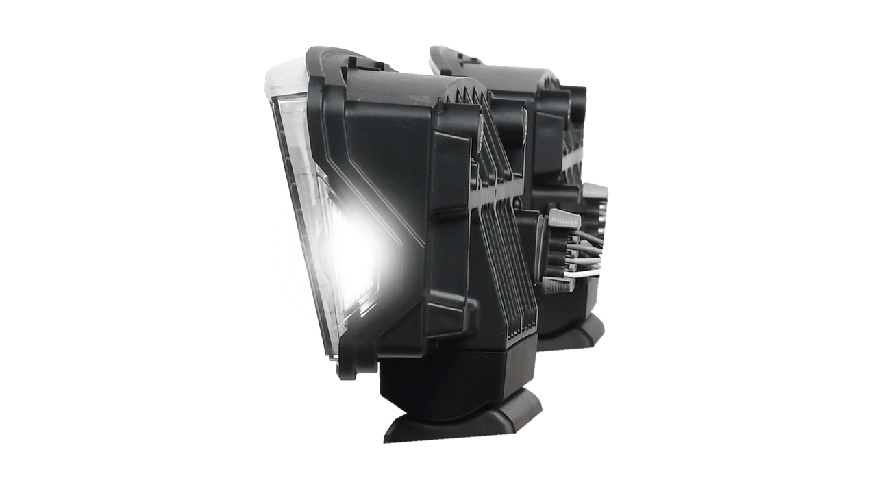 Side view of two black rectangular LED vehicle headlights with cooling fins and wiring connectors, shown against a white background. One headlight is illuminated, emitting a bright white light.
