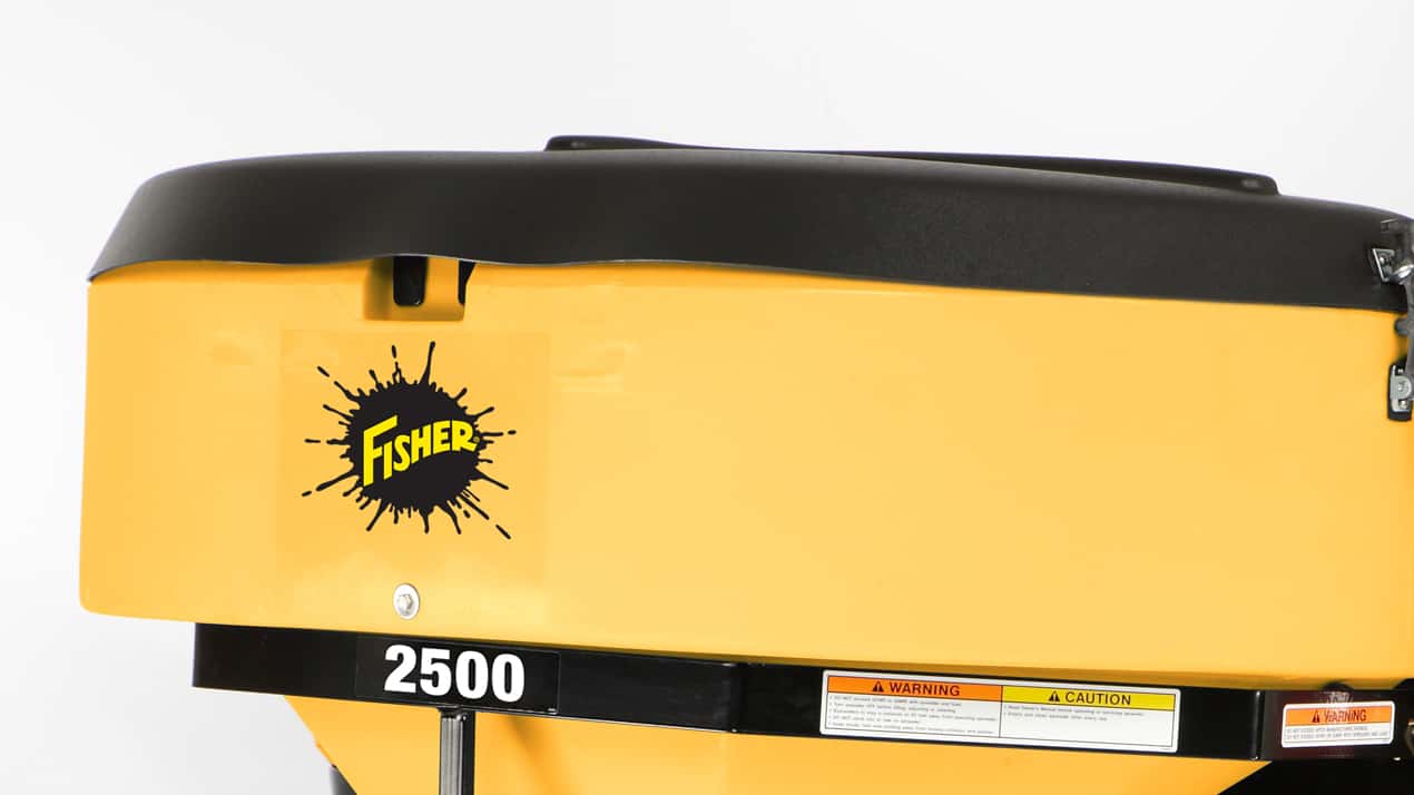 Close-up of a yellow Fisher 2500 salt spreader with a black lid. The Fisher logo and caution labels are visible on the side against a plain white background.