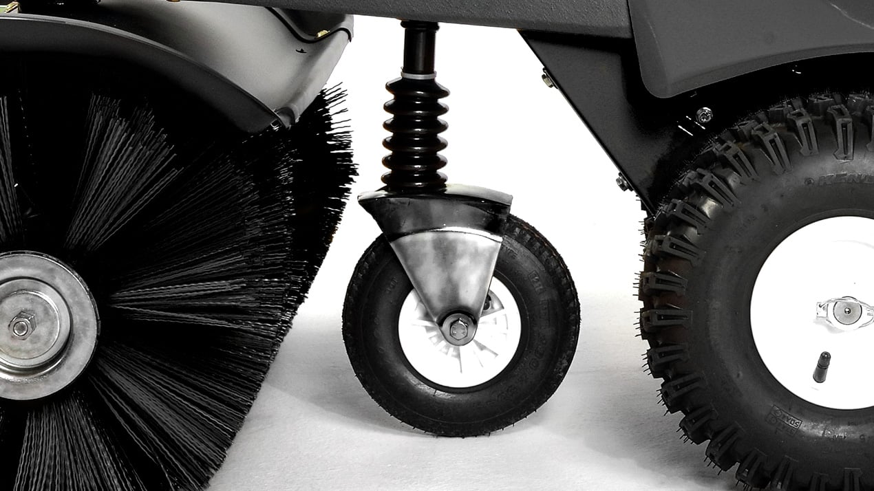 Close-up of three wheels on a cleaning machine: a large bristled brush wheel on the left, a small swivel caster wheel in the center, and a large rubber tire on the right, all set against a white background.