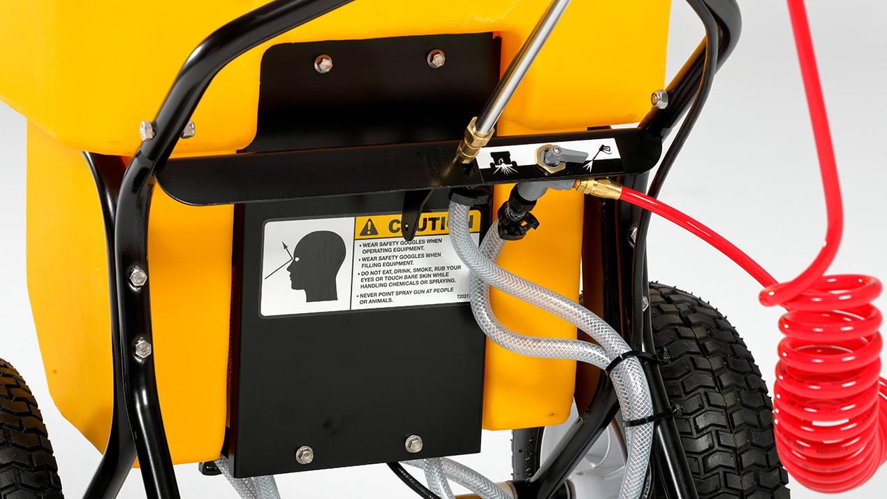 Close-up of a yellow and black wheeled machine with warning labels, a coiled red air hose, and gray and black cables attached, possibly part of industrial or workshop equipment.