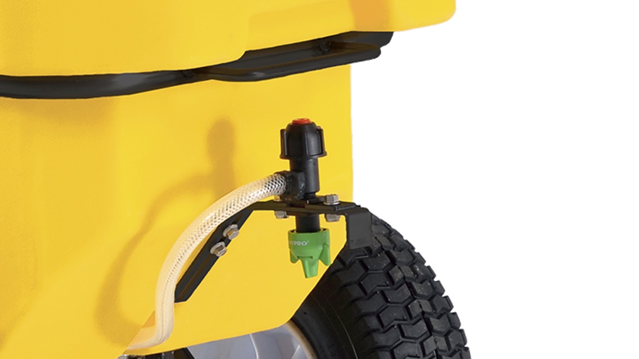 Close-up of a yellow wheeled container showing a hose attached to a valve or nozzle near one of its black rubber wheels. The setup appears to be part of a spraying or dispensing system.