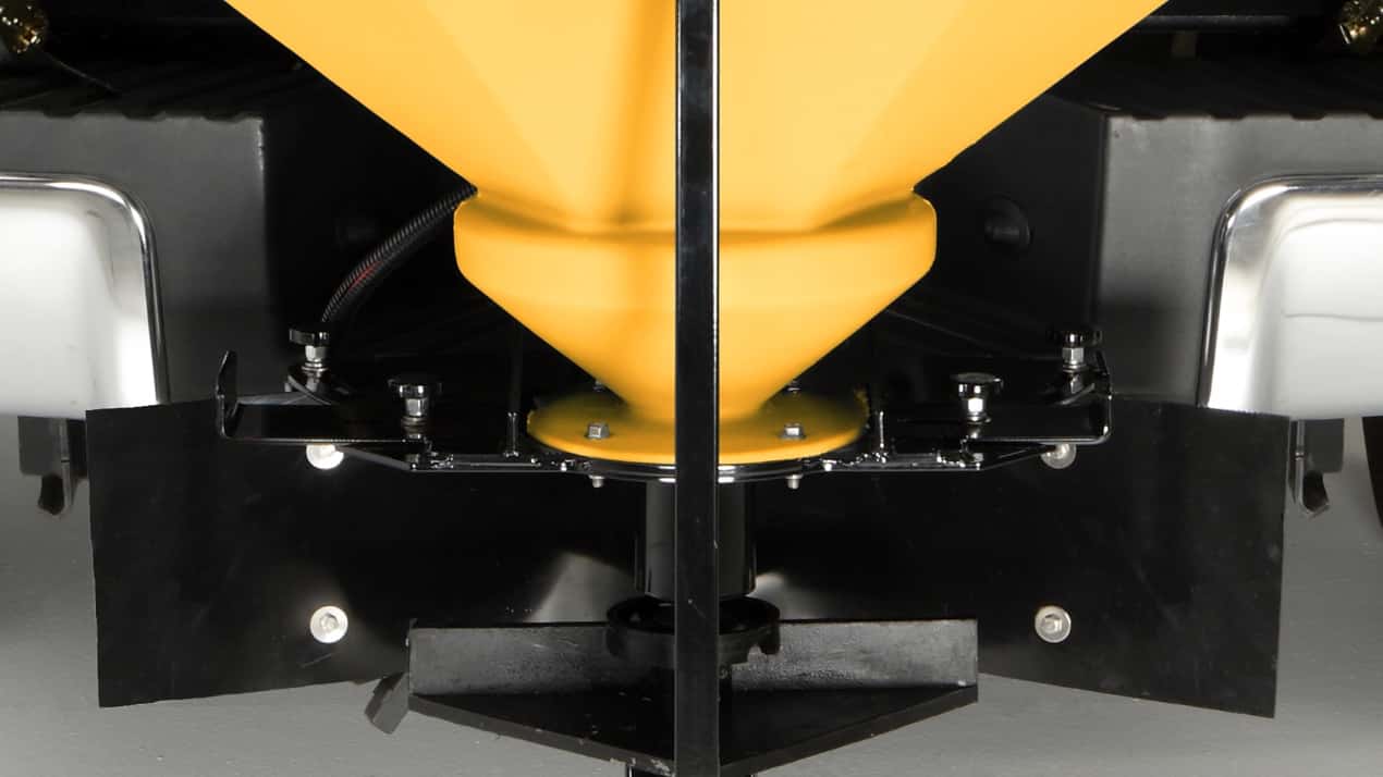 Close-up of the back of a vehicle showing a yellow hopper or spreader used for distributing materials like salt or sand, with metal components and black guards on either side.