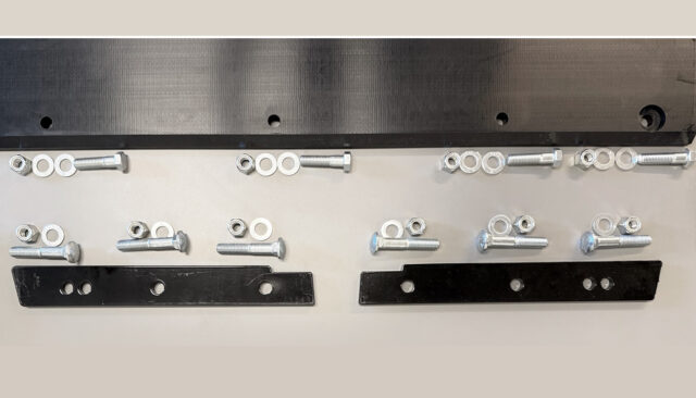Various metal bolts, nuts, and washers are neatly arranged on a flat surface alongside two black metal brackets with holes, and a larger black component at the top of the image.