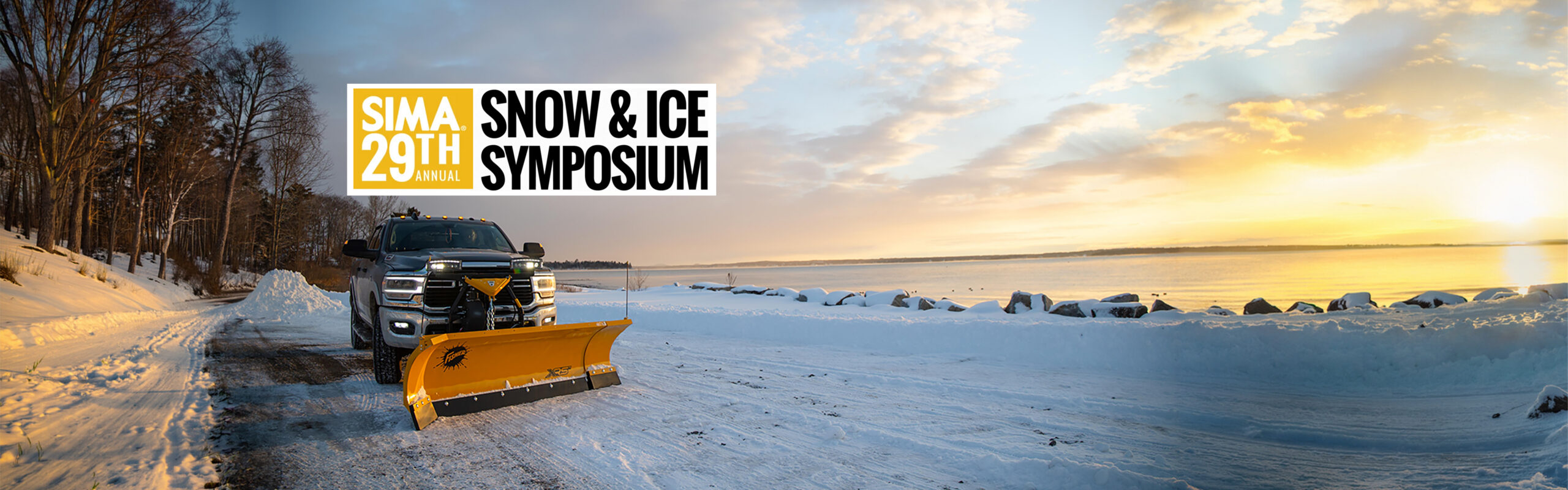 A snowplow truck clears a snowy lakeside road at sunrise. To the left, trees line the road; to the right, the lake is bordered by snow and rocks. A banner reads “SIMA 29th Annual Snow & Ice Symposium.”.